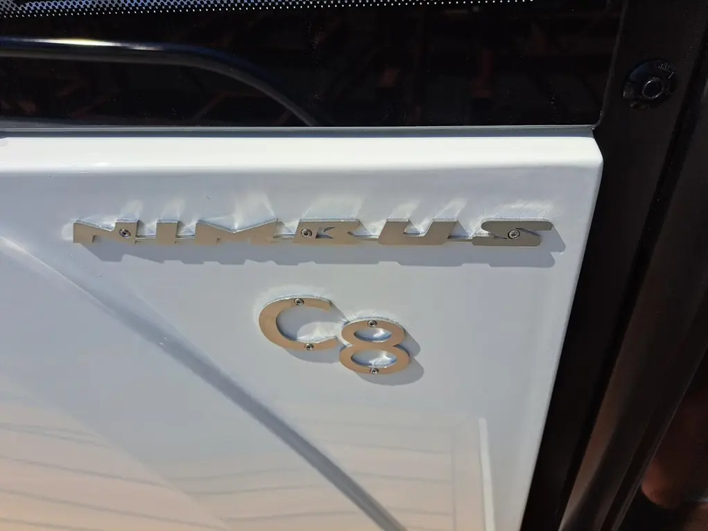 White door of a Nimbus C8 boat, featuring the metallic 'NIMBUS' logo and 'C8' model number, reflecting sunlight.